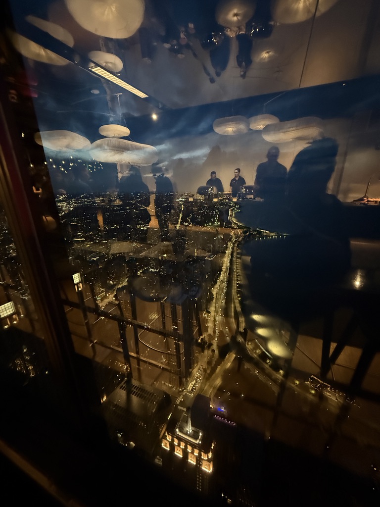 Blick bei Nacht aus einem Hochhaus auf die beleuchteten Straßen der Stadt, mit Spiegelungen im Fenster